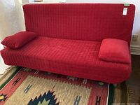 Front view of red futon sofa with quilted velvet-like fabric and two matching cushions.