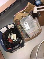 Overview of two boxes showing assorted hand tools and accessories alongside coiled electrical extension cords mostly black with orange connectors.