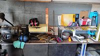 Workbench cluttered with various tools including drill, sheet sander, wrenches, pliers, and other accessories