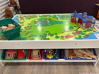 Front view of wooden train table with printed landscape top and lower shelf with four storage bins