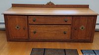 Front view of oak storage bench showing two dovetailed drawers and two side cabinet doors with carved medallions and round brass knobs, decorative back rail.