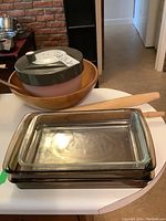 Large wooden salad bowl with plastic salad spinner on top, two wooden rolling pins behind, and three clear rectangular bakeware dishes stacked in front