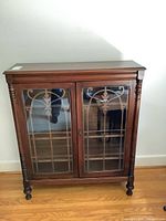 Front view of vintage mahogany bookcase with two decorative glass doors and carved details, showing overall structure and finish.