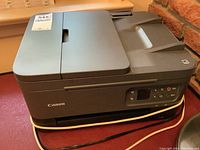 Canon Pixma flatbed printer showing top lid and power cord wrapped around base.