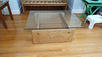 Full view of coffee table showing clear glass top over light wood base on hardwood floor
