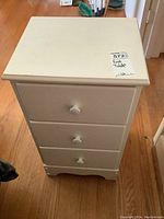 Front view of the off-white painted wood end table with three drawers showing white round knobs and worn paint.