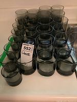 26 pieces of vintage smoked glassware arranged in rows on a counter, showing three sizes of tumblers.