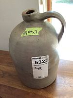 Front view of the antique pottery jug showing the large rounded body with handle and spout. Sticker label shows indicated dimensions.