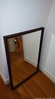 Full view of the vintage mirror leaning against the wall showing the front reflective surface and wood frame.