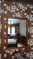 Wall mounted rectangular mirror with a medium tone maple wood frame reflecting a floral wallpapered room.