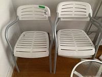 Front view of two white slatted patio chairs with metal frames showing wear and dirt.