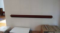 Walnut plate rail mounted high on a white wall above storage boxes, shows full length and wood grain finish.