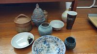 Photo showing a variety of pottery items including bowls, vases, cups, and cannisters arranged on a wooden surface.