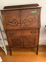 Front view of vintage oak secretary desk showing carved front panel, one drawer, two doors, and original hardware.
