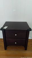 Front view of wood side table with two drawers and metal pulls, showing dark wood finish and rectangular shape.