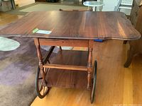 Full view of rectangular fruitwood tea cart with carved edges, large spoked wooden wheels, and lower shelf.