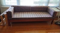 Front view of vintage wood sofa bed with patterned cushions, showing geometric and abstract print upholstery and wooden frame.