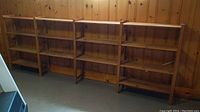 Four connected wood shelving units against wood paneled wall in basement room with concrete floor. Each shelving unit has four shelves and are attached side-by-side.