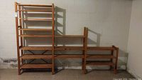 Wide angled photo of three wood shelving units set against a basement concrete block wall showing different heights and shelf counts.