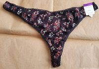Front view of black bikini underwear with floral print and lace trim, showing full shape and elastic waistband with tag attached