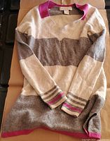 Front view of cashmere sweater showing pink, beige and taupe stripes with pink collar and cuffs.