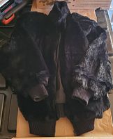 Front view of black faux fur women's jacket laid flat showing zippered front and ribbed cuffs and waistband.