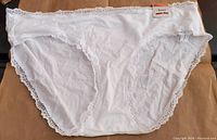 Front view of white cotton hipster underwear with lace trim, brand tag visible.
