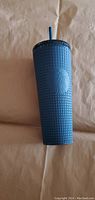 Tall blue textured Starbucks cup standing upright showing front embossed logo and surface texture.