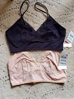 Lot includes two medium size bras by International Concepts in black and light peach, both new with tags, displayed on carpet.