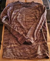 Brown camouflage long sleeve sweatshirt laid flat on brown cloth, showing full front view