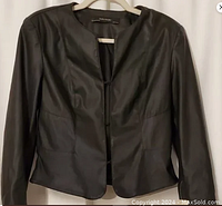 Front view of Zara Basics black pleather jacket with long sleeves and no collar, hanging on a hanger.
