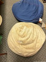 Two bean bag lounge seats, one navy blue and the other cream faux fur, placed on carpeted floor.