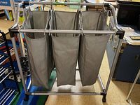 Full view of the 3-section laundry hamper with three beige fabric bags hanging from metal frame.