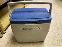 Front view of the Coleman Oscar cooler, showing beige body and blue lid with Coleman Oscar logo on front.