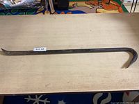 Full length image of a crow bar lying on a wooden table, showing the hooked end and overall shape.