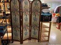 Full view of 3 panel decorative screen in basement storage, showing floral fabric inserts and wooden arched frames with brass hinges.