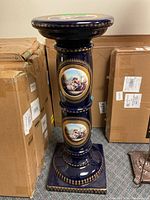 Full view of the decorative ceramic plant stand showing hand-painted classical scenes and gold accents.