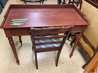 Photo showing the front side of the wood desk with raised edges and turned legs along with the wooden chair in front
