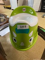 Front view of the green dinosaur-themed Fisher Price potty chair with Lot 6 label on the front.