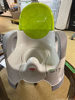 Close-up of the Fisher Price potty chair showing the white base and green backrest, in good condition on a table.
