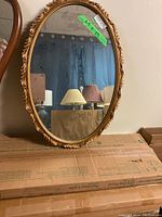 Photo of the oval mirror showing its reflective surface and the ornate golden frame with leaf and scroll details.