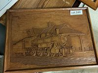 Wood carved framed panel showing a train locomotive at station scene, lot label visible