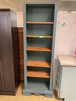 Full view of the tall bookshelf showing painted sides and multiple natural wood shelves inside.