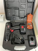 Black Jobmate cordless drill with battery, charger, and small orange accessory box inside molded plastic case.