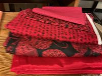 Red fabrics folded on wooden surface, solid red and black/red patterned with paisley design