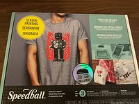 Front of box showing Speedball screen printing kit, man wearing robot print shirt, text indicating LED lamp included and level 3 photo emulsion stencil kit.
