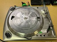 Full view of Numark professional turntable with platter and connected accessory cords on a wood surface.