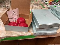 Photo showing open box with 3 red spherical tea light candles inside, PartyLite Aroma Melt branding visible on packaging.