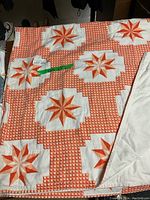 Overall view of the quilt showing orange starburst patterns on a white and orange checked background.