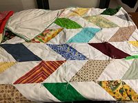 Full view of quilt spread out showing multicolored diamond patchwork pattern sewn onto white fabric.